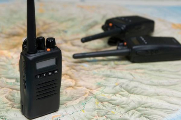 Three black radios with an orange button are lying on top of a map depicting geographical features.