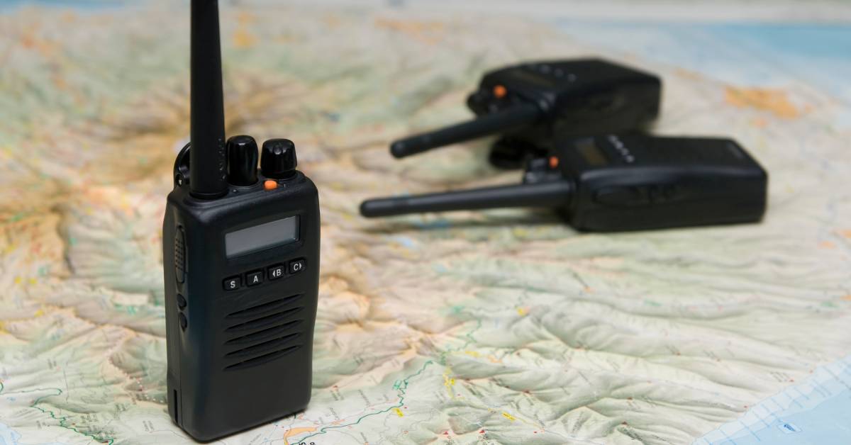 Three black radios with an orange button are lying on top of a map depicting geographical features.