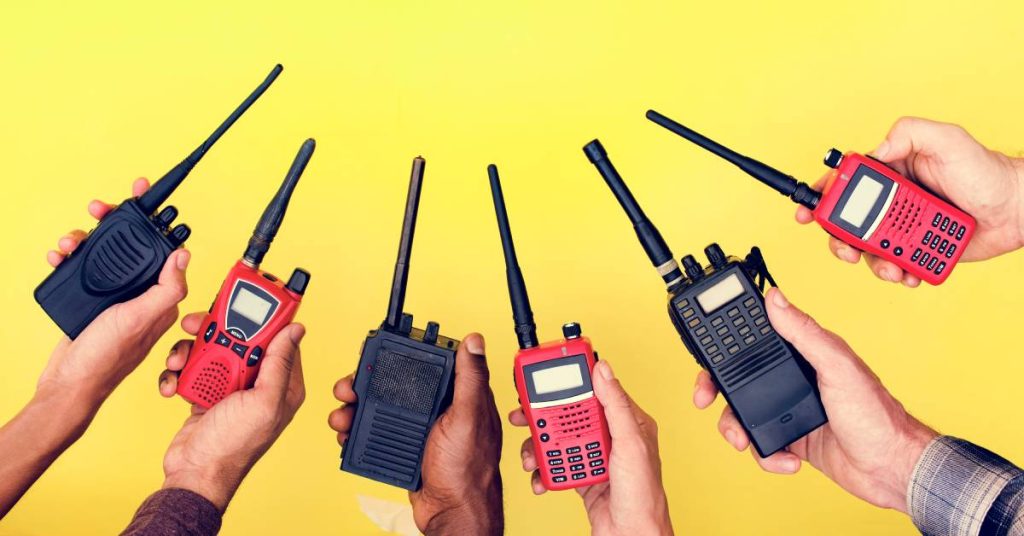 A group of hands hold out alternating black and red two-way radios in the shape of an arc over a yellow background.