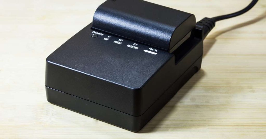 A black battery inserted into a battery charger with a cord coming off it sitting on top of a wooden table.