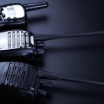 Three black two-way radios sitting next to one another over a black background with a light shining on them.