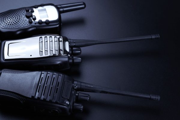 Three black two-way radios sitting next to one another over a black background with a light shining on them.