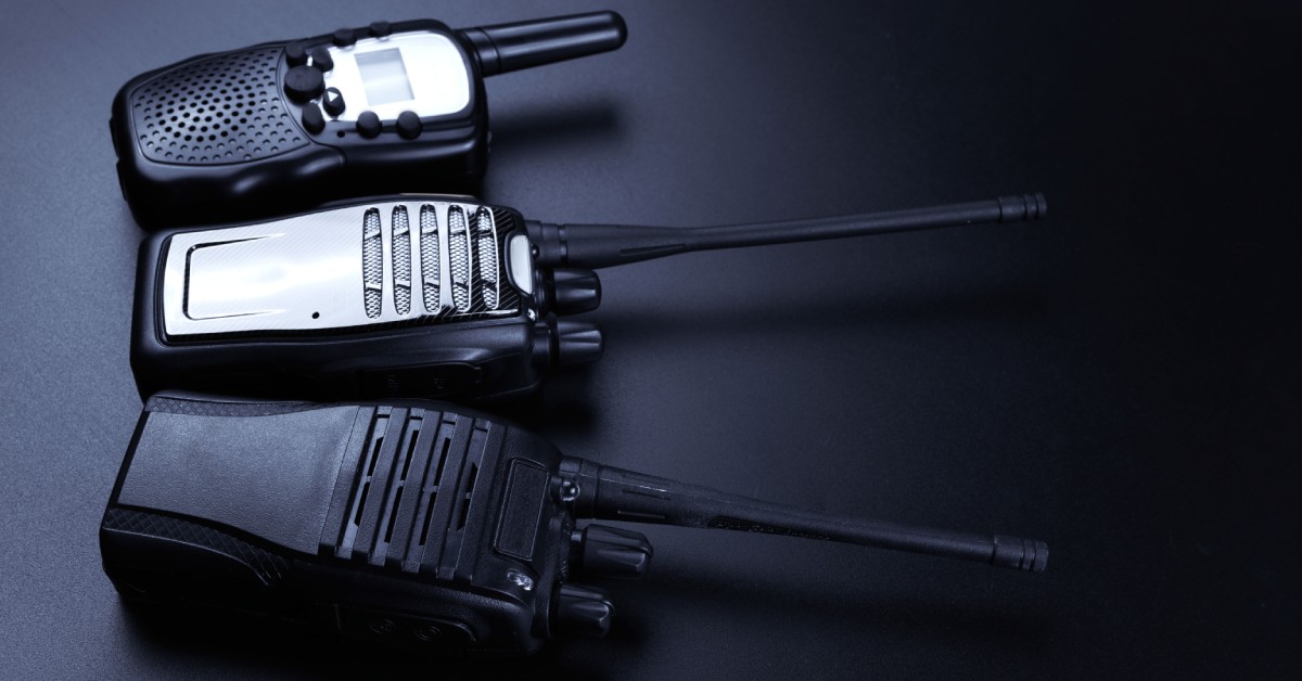 Three black two-way radios sitting next to one another over a black background with a light shining on them.