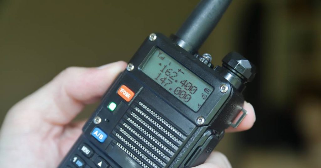 Someone holding a two-way radio with orange and blue buttons at close range. The screen displays 162.400 and 147.000.