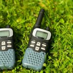 A close-up of two black two-way radios with white buttons and green speakers lying in the grass.