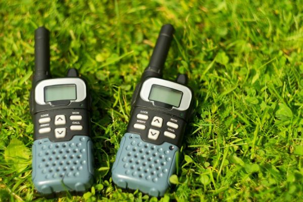 A close-up of two black two-way radios with white buttons and green speakers lying in the grass.