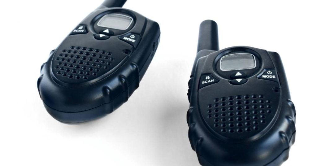 A couple of black two-way radios with white buttons that say "Scan and Mode" sitting in front of an empty background.