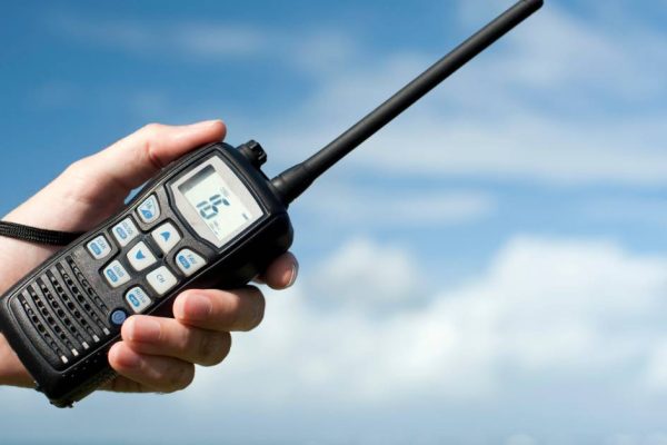 A person’s hand holding a black two-way radio with a strap on it. The screen shows the number "16".