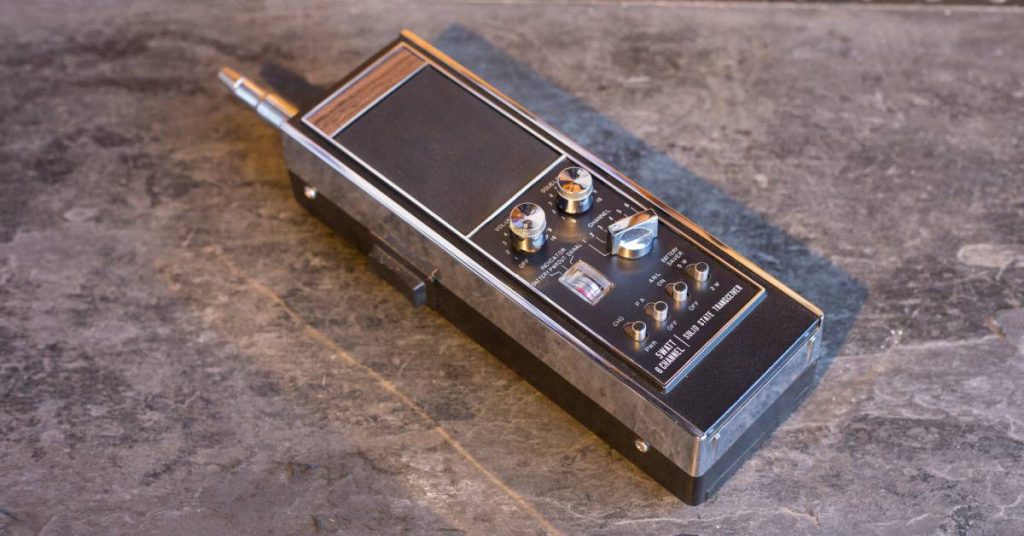 A two-way radio made of reflective metal with knobs and dials sitting on a table with a marble surface.