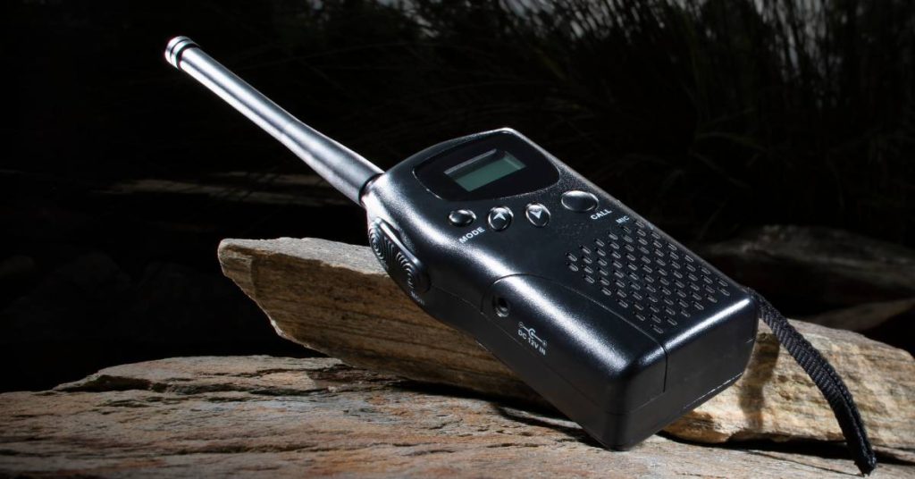 A black two-way radio with a strap on it sits on top of a couple of large rocks with a dark sky in the background.

