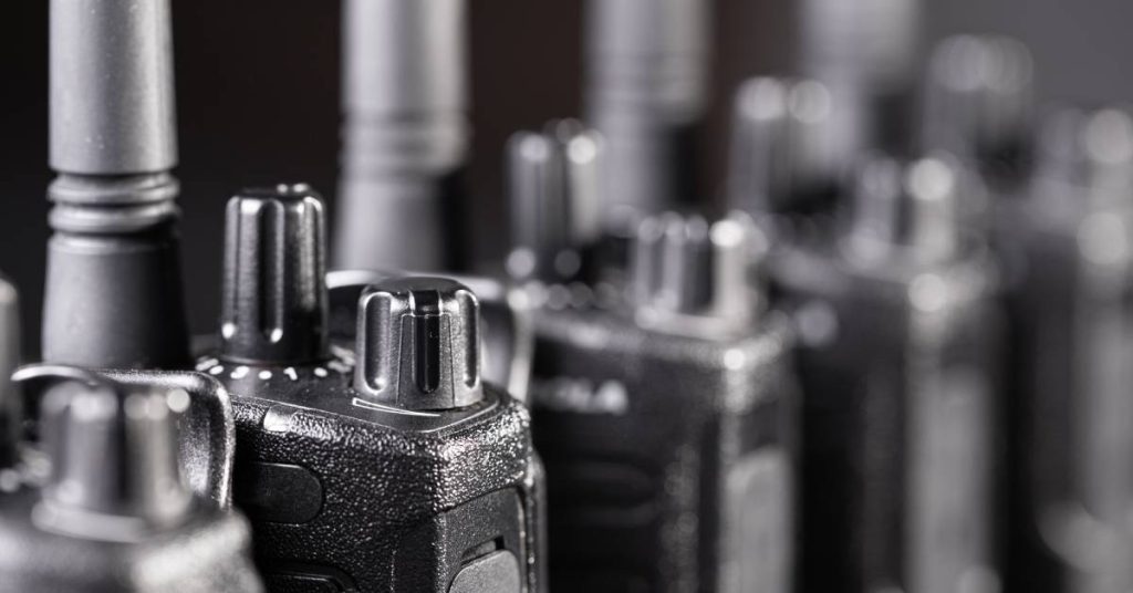 A row of walkie-talkies next to one another with white highlights on their surface sits over a black background.