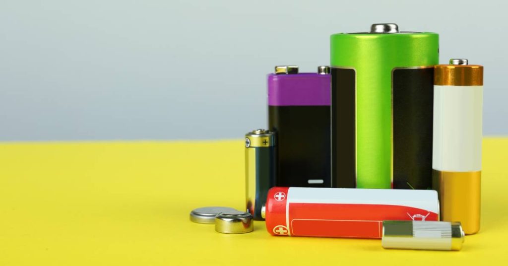 A group of batteries with different cell types sitting together on a yellow surface with a gray wall in the background.