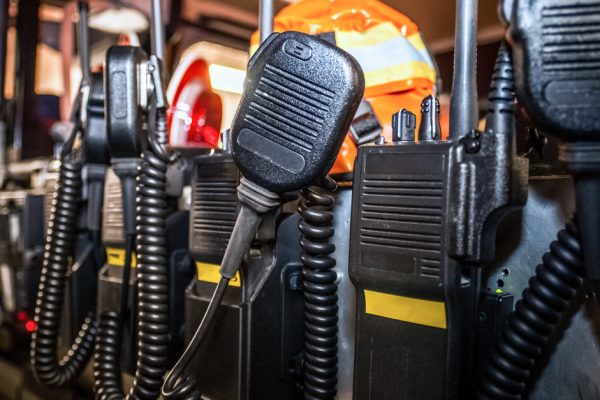 The backseat of an emergency responder vehicle contains a group of black, two-way communication radios.