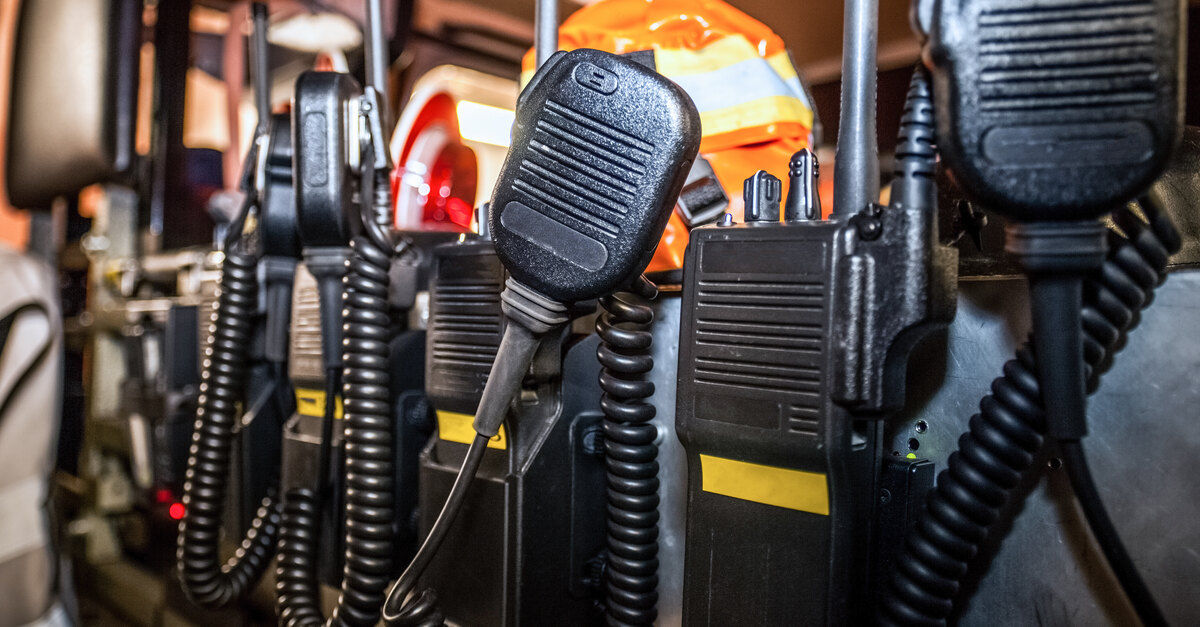 The backseat of an emergency responder vehicle contains a group of black, two-way communication radios.