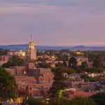 An aerial view of Santa Fe, New Mexico, shows the city’s brick buildings, twinkling lights, and gorgeous skyline.