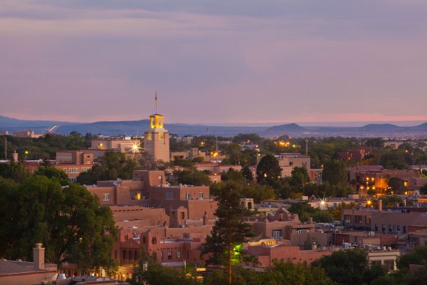 An aerial view of Santa Fe, New Mexico, shows the city’s brick buildings, twinkling lights, and gorgeous skyline.